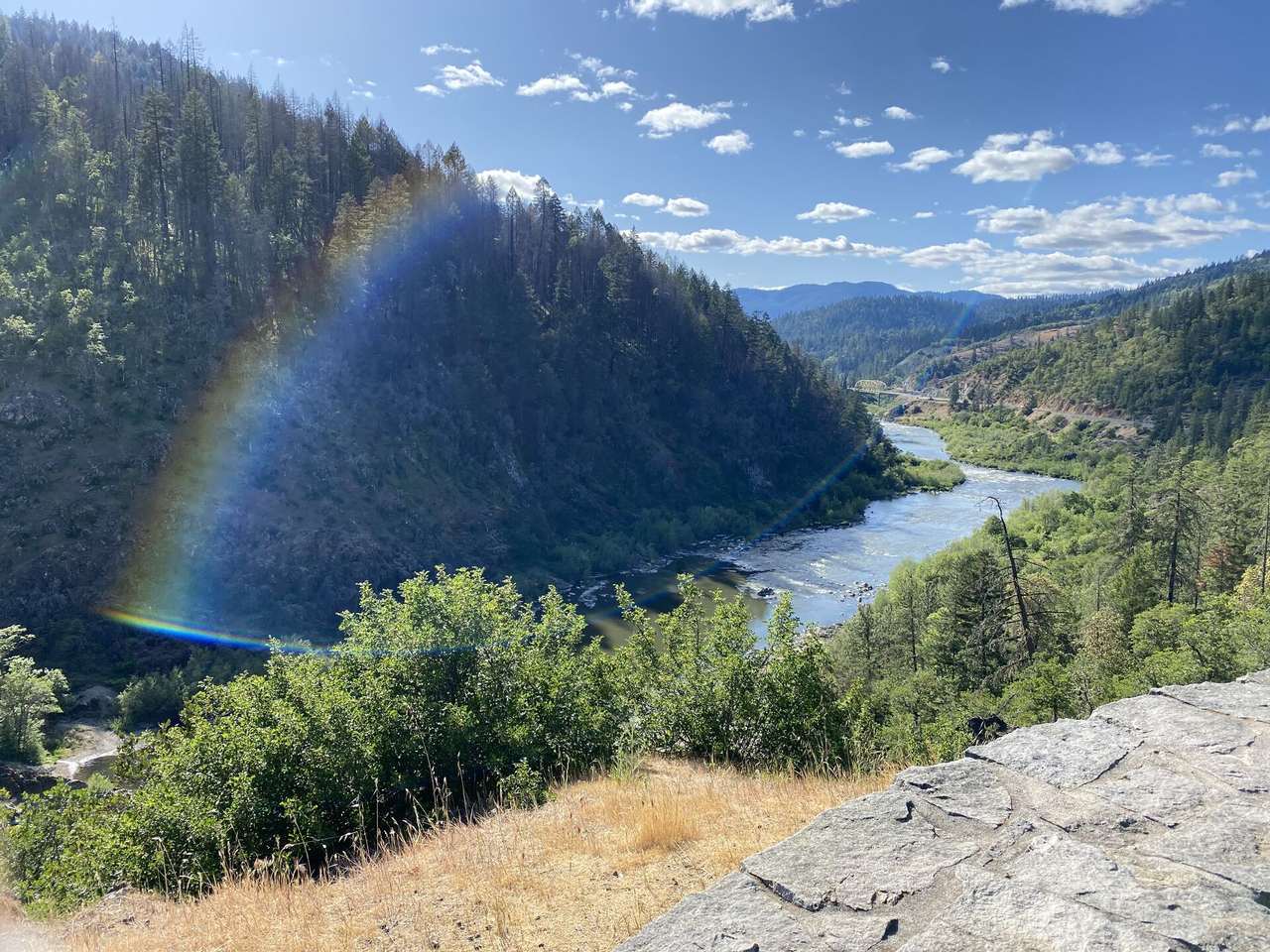 A rainbow arching over a forested river canyon